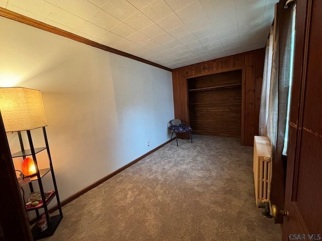 unfurnished bedroom featuring ornamental molding, radiator heating unit, dark carpet, and wood walls