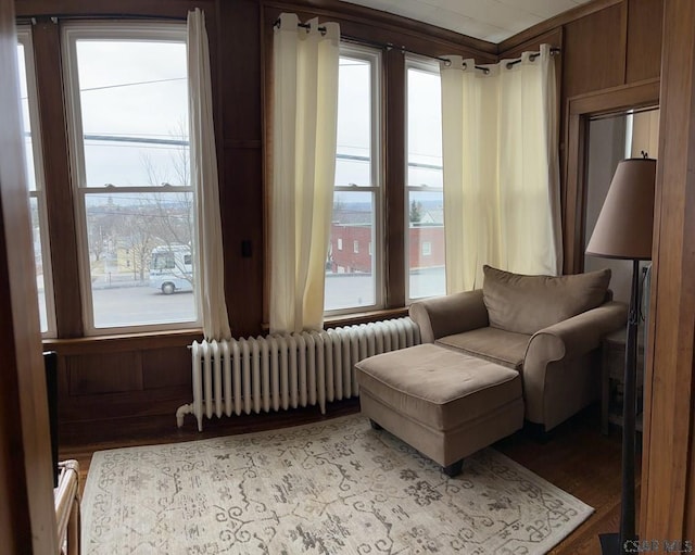 living area featuring radiator heating unit, light wood-type flooring, and wood walls