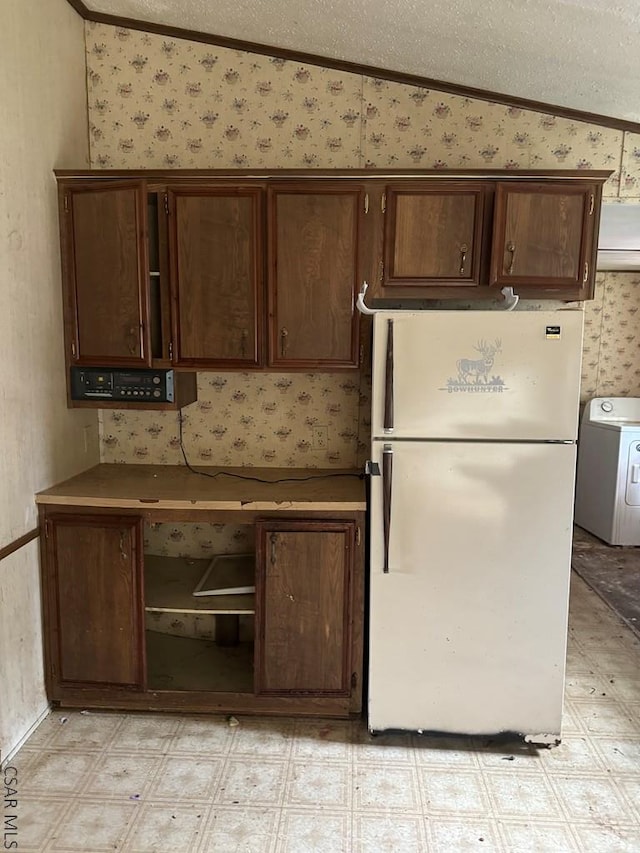 kitchen featuring vaulted ceiling, washer / dryer, white refrigerator, crown molding, and a textured ceiling