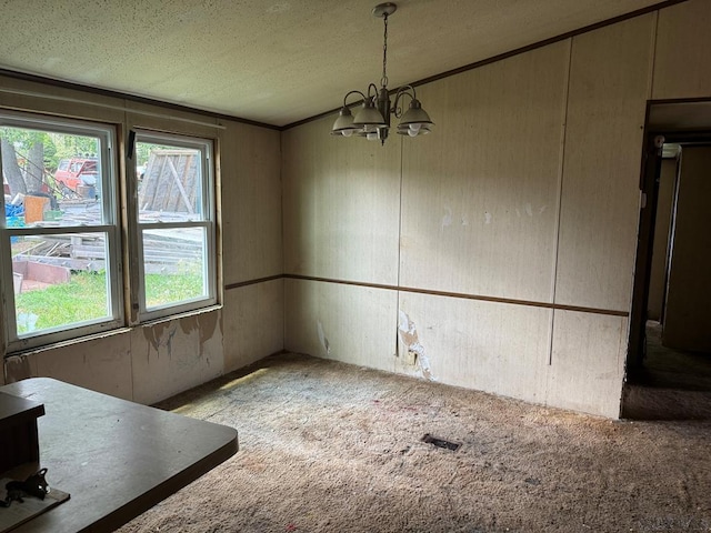 unfurnished dining area with a textured ceiling, ornamental molding, a chandelier, and carpet