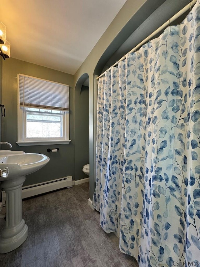 bathroom with toilet, sink, wood-type flooring, curtained shower, and a baseboard heating unit