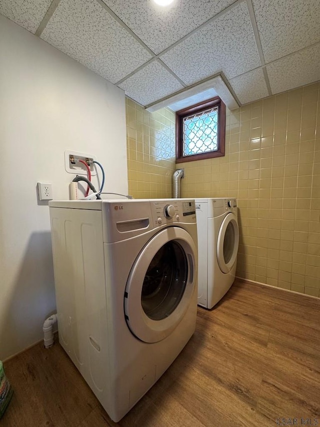 clothes washing area with wood-type flooring, tile walls, and washing machine and dryer