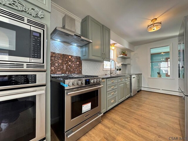 kitchen with appliances with stainless steel finishes, sink, backsplash, wall chimney exhaust hood, and light hardwood / wood-style flooring