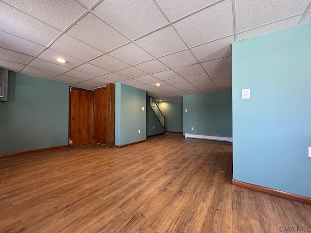 interior space with a drop ceiling, a baseboard heating unit, and hardwood / wood-style floors