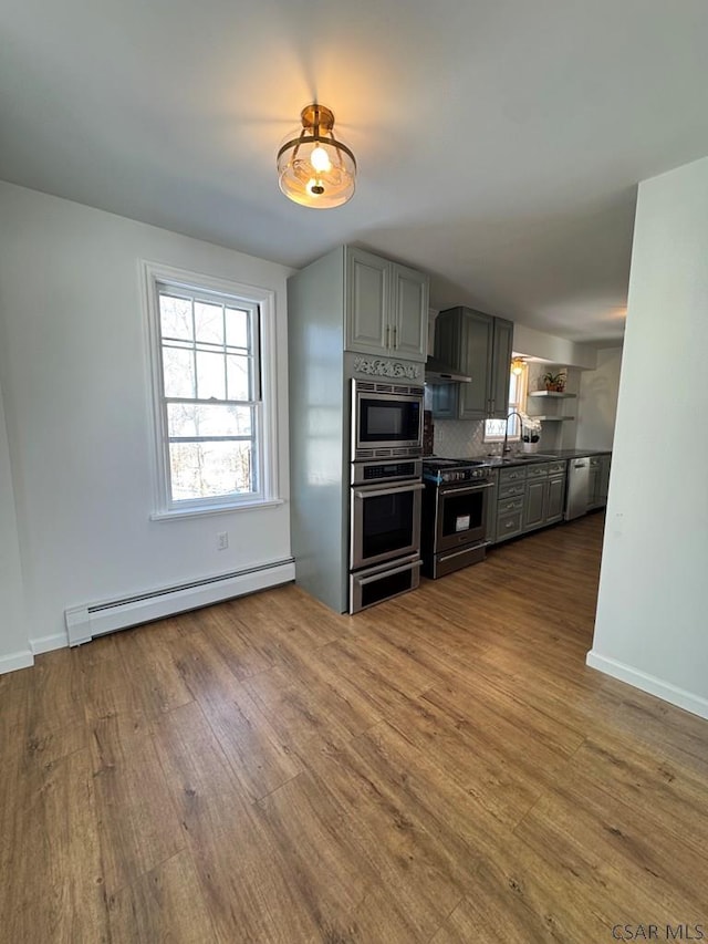 kitchen featuring appliances with stainless steel finishes, gray cabinets, hardwood / wood-style floors, and a baseboard heating unit