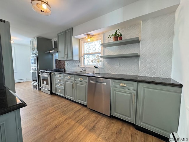 kitchen with sink, appliances with stainless steel finishes, a baseboard heating unit, backsplash, and light hardwood / wood-style floors