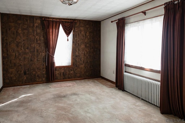 unfurnished room featuring radiator heating unit, wooden walls, light carpet, and a wealth of natural light