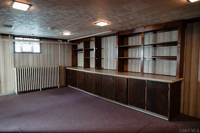 basement featuring radiator, dark carpet, and wood walls