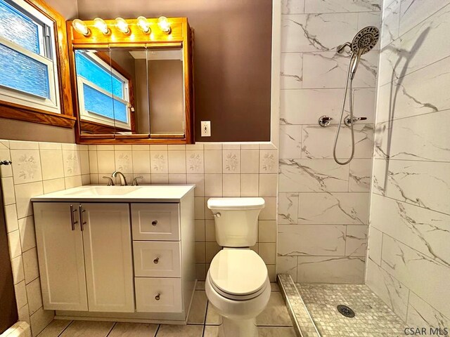 bathroom featuring tile walls, tiled shower, vanity, tile patterned floors, and toilet