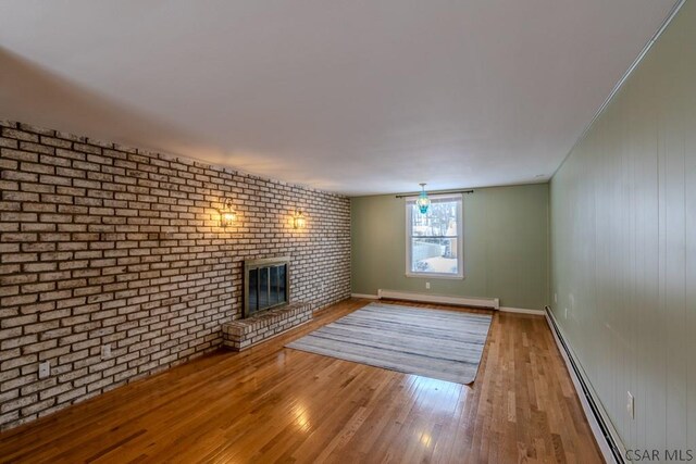 unfurnished living room featuring light wood-type flooring, a brick fireplace, a baseboard radiator, and brick wall