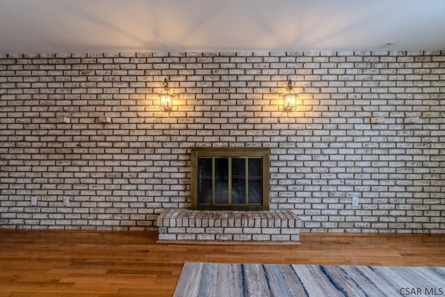 unfurnished living room featuring a fireplace, wood-type flooring, and brick wall