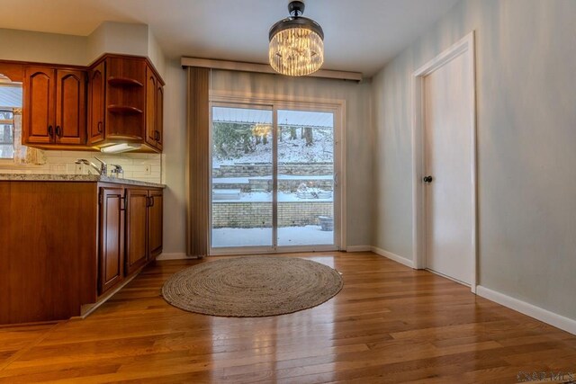 kitchen with wood-type flooring, light stone counters, backsplash, and an inviting chandelier