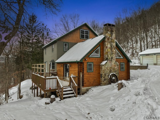 snow covered back of property featuring a wooden deck and a garage