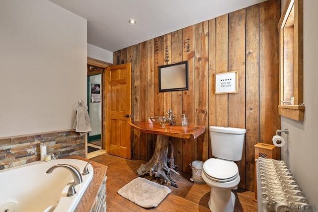 bathroom featuring a bathing tub, radiator, hardwood / wood-style floors, wood walls, and toilet