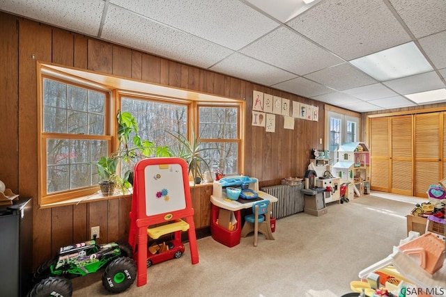 game room featuring carpet flooring, a drop ceiling, and wood walls