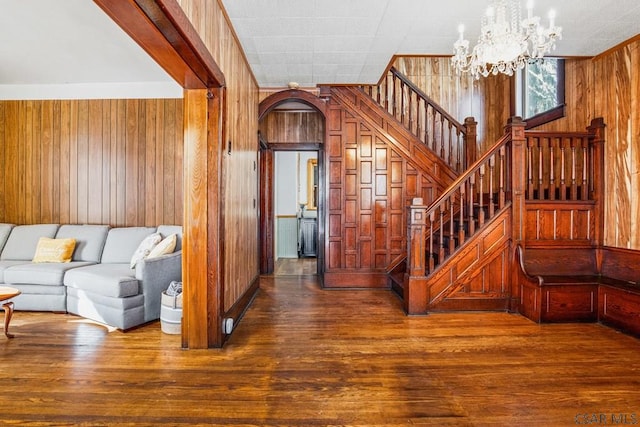 stairs featuring an inviting chandelier, wooden walls, and wood-type flooring