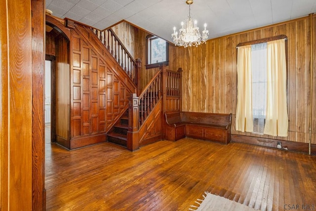 unfurnished living room featuring wood-type flooring, wooden walls, and a chandelier