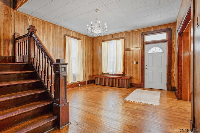 entryway featuring an inviting chandelier, radiator heating unit, wooden walls, and light wood-type flooring