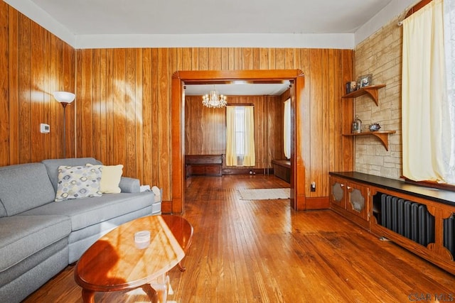 living room with a notable chandelier, hardwood / wood-style flooring, radiator heating unit, and wood walls