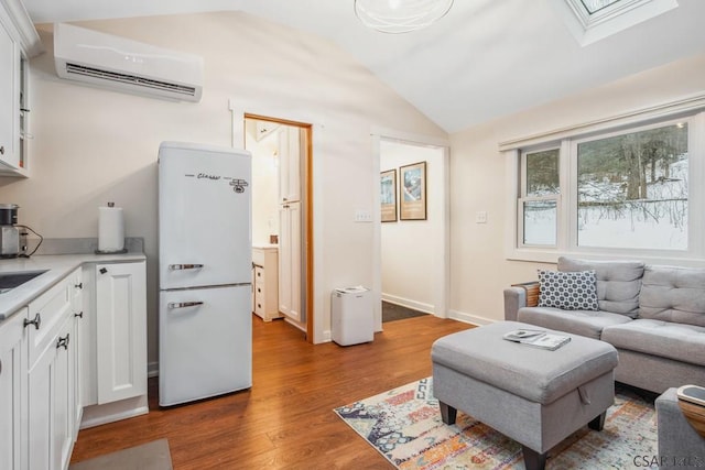 living area featuring lofted ceiling with skylight, a wall mounted air conditioner, baseboards, and wood finished floors