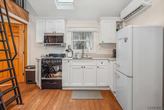 kitchen featuring white cabinets, stainless steel microwave, freestanding refrigerator, light countertops, and an AC wall unit