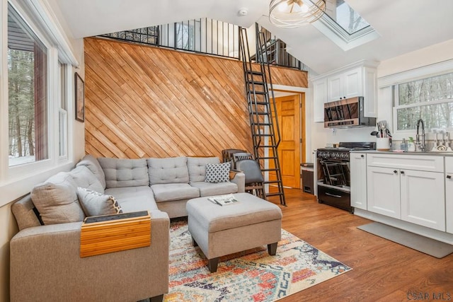 living area with lofted ceiling with skylight, light wood-type flooring, and wooden walls