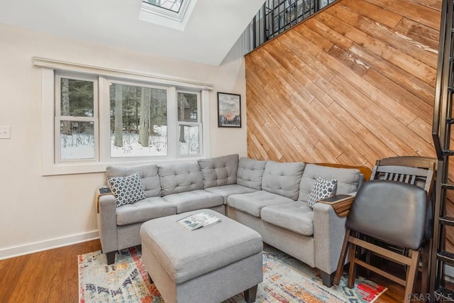 living area with lofted ceiling with skylight, wooden walls, baseboards, and wood finished floors