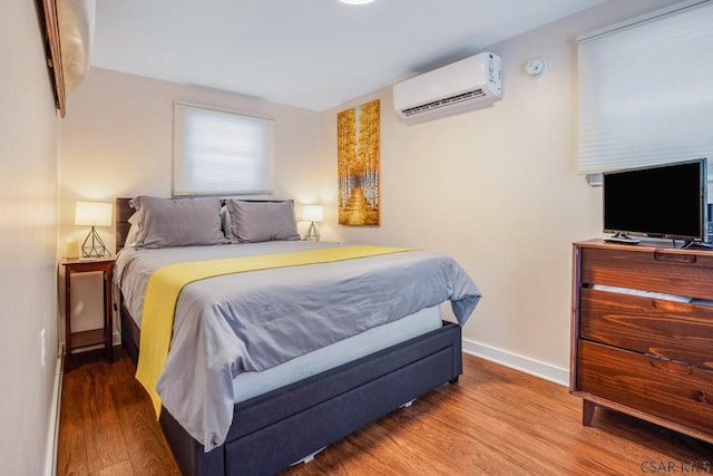 bedroom featuring a wall unit AC, baseboards, and wood finished floors