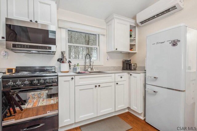 kitchen with a sink, light countertops, freestanding refrigerator, stainless steel microwave, and a wall mounted air conditioner