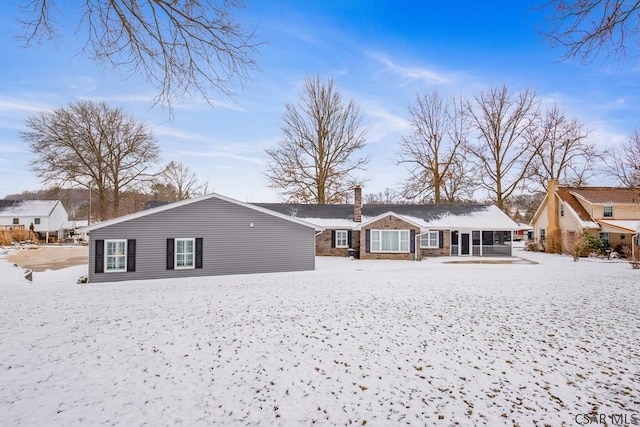 snow covered rear of property featuring a chimney and a sunroom