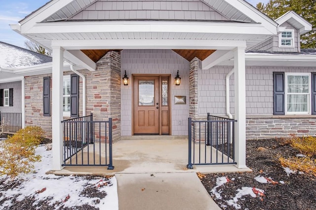 doorway to property featuring stone siding, roof with shingles, and covered porch