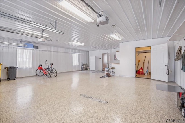 garage with a garage door opener, metal wall, and freestanding refrigerator