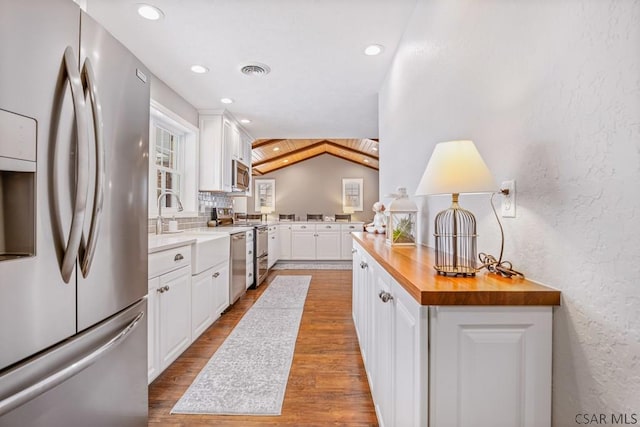 kitchen featuring butcher block countertops, appliances with stainless steel finishes, white cabinets, and a textured wall