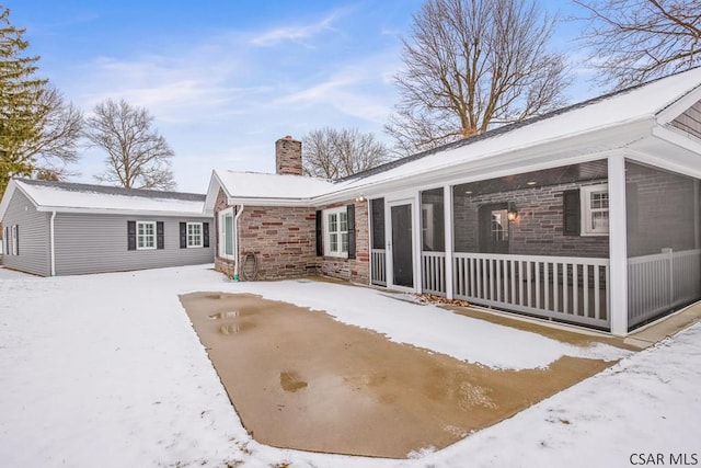 snow covered house featuring a chimney and a sunroom