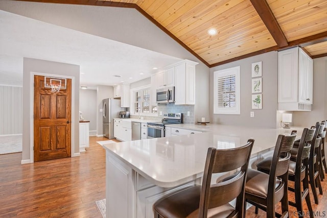 kitchen with light wood-type flooring, light countertops, lofted ceiling with beams, appliances with stainless steel finishes, and a peninsula