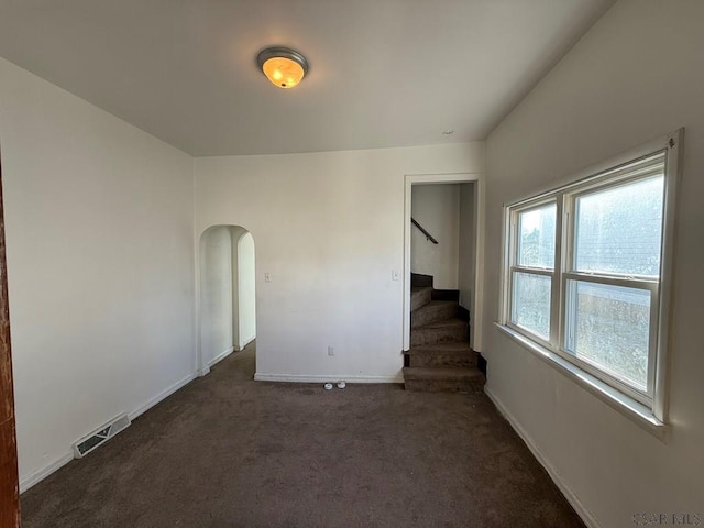 spare room featuring arched walkways, visible vents, dark carpet, stairway, and baseboards