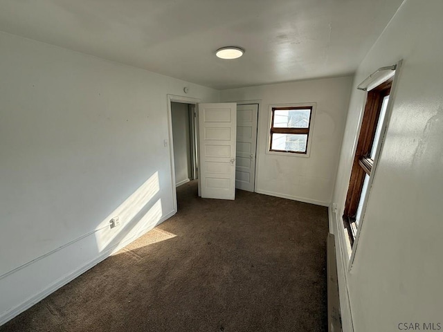 unfurnished bedroom with baseboards, dark carpet, and a closet