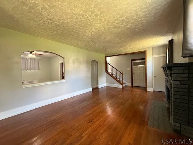 106 Lucetta St, Johnstown, PA 15905 - unfurnished living room featuring a brick fireplace, a textured ceiling, arched walkways, wood finished floors, and a ceiling fan