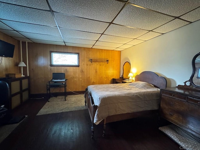 bedroom featuring dark hardwood / wood-style flooring, a drop ceiling, and wooden walls