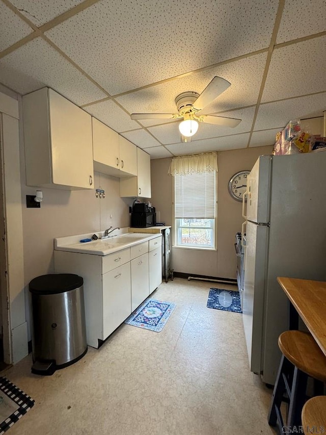 kitchen with sink, white cabinets, white refrigerator, ceiling fan, and a drop ceiling