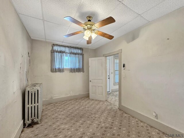 carpeted empty room featuring radiator, a paneled ceiling, and ceiling fan