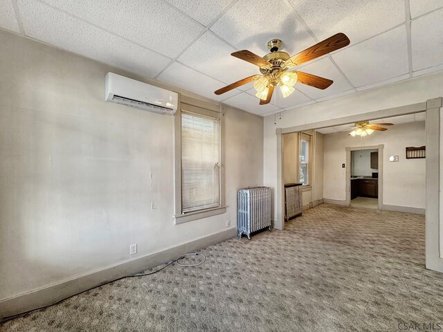 carpeted spare room with radiator, a wall mounted AC, a drop ceiling, and ceiling fan