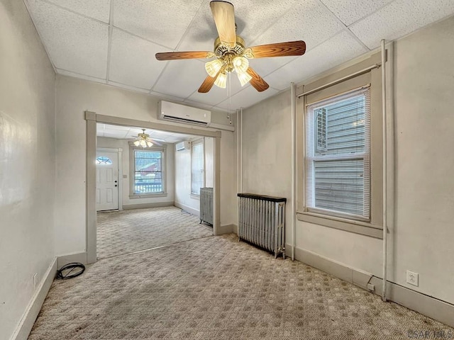 carpeted spare room with radiator heating unit, a wealth of natural light, a paneled ceiling, and a wall mounted AC