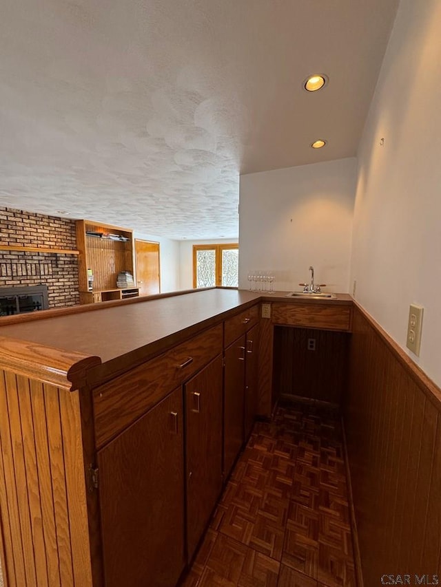 bar with wood walls, sink, dark parquet flooring, a brick fireplace, and a textured ceiling