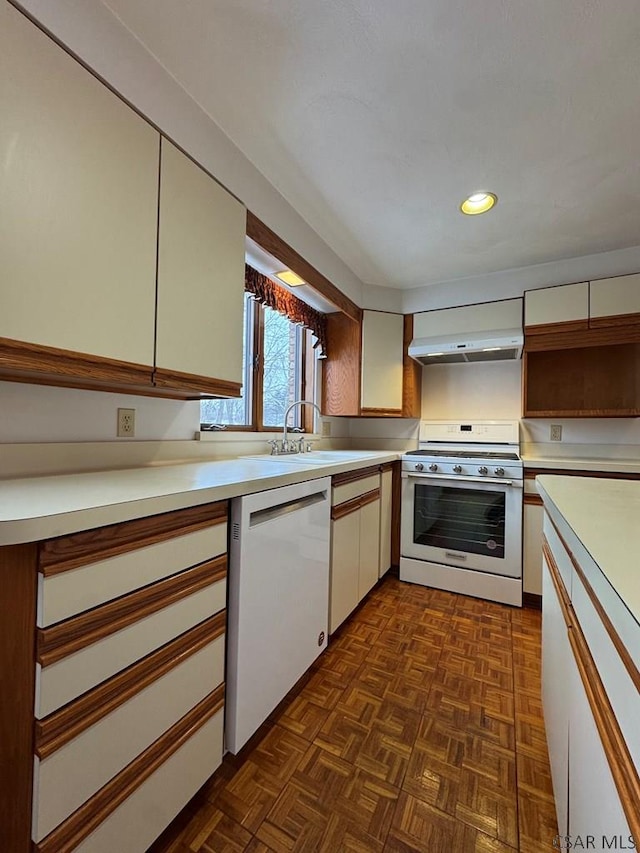 kitchen featuring wall chimney range hood, sink, range, white dishwasher, and dark parquet flooring