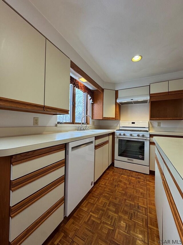 kitchen featuring wall chimney range hood, sink, range, white dishwasher, and dark parquet flooring