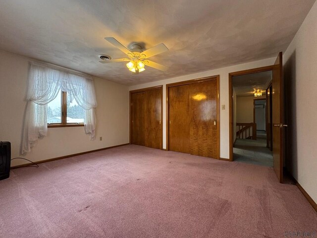 unfurnished bedroom featuring ceiling fan, carpet floors, and two closets