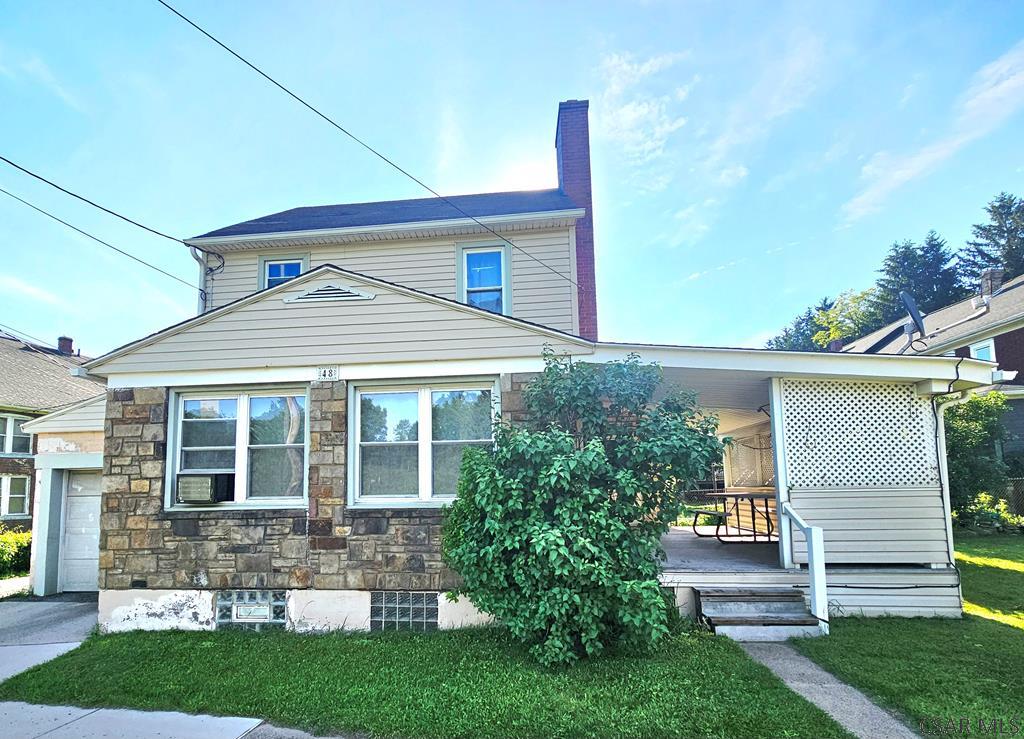 48 D St, Johnstown, PA 15906 - view of front of property featuring stone siding, a chimney, a front yard, an attached garage, and a porch