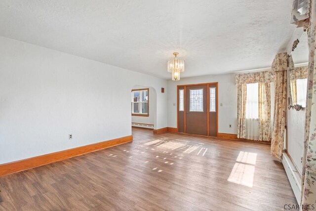 unfurnished room featuring a notable chandelier, wood-type flooring, a textured ceiling, and a baseboard heating unit