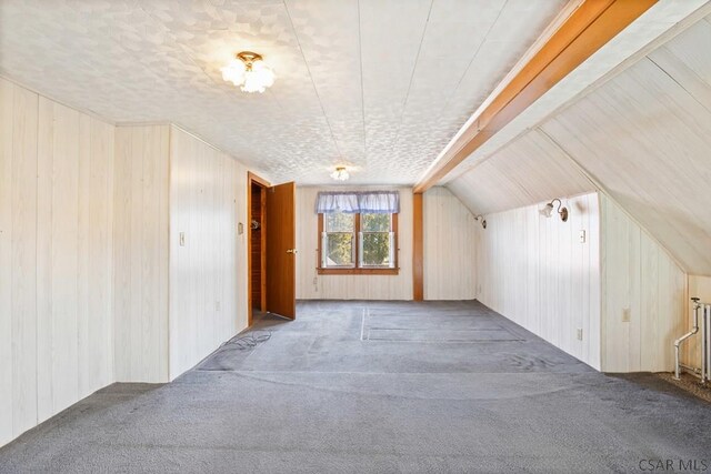 additional living space with vaulted ceiling, carpet flooring, and wood walls